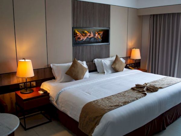 A stylish hotel bedroom with a lit fireplace, bedside lamps, and neatly made beds with pillows and a folded blanket.