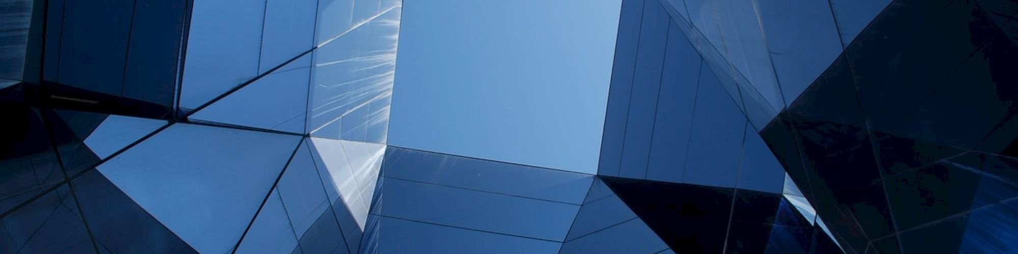 A close-up of a futuristic blue glass building facade with angular panels and glowing reflections.
