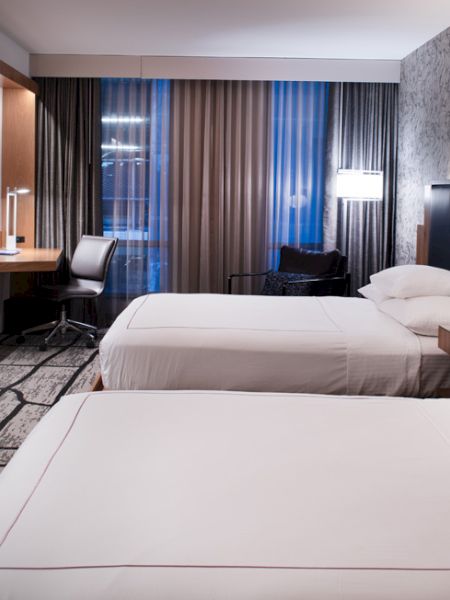 Modern hotel room: two beds, wall TV, patterned carpet, and curtains with blue light from outside.