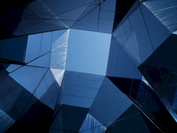 Blue glass skyscraper facade with geometric panels and sharp angular reflections.