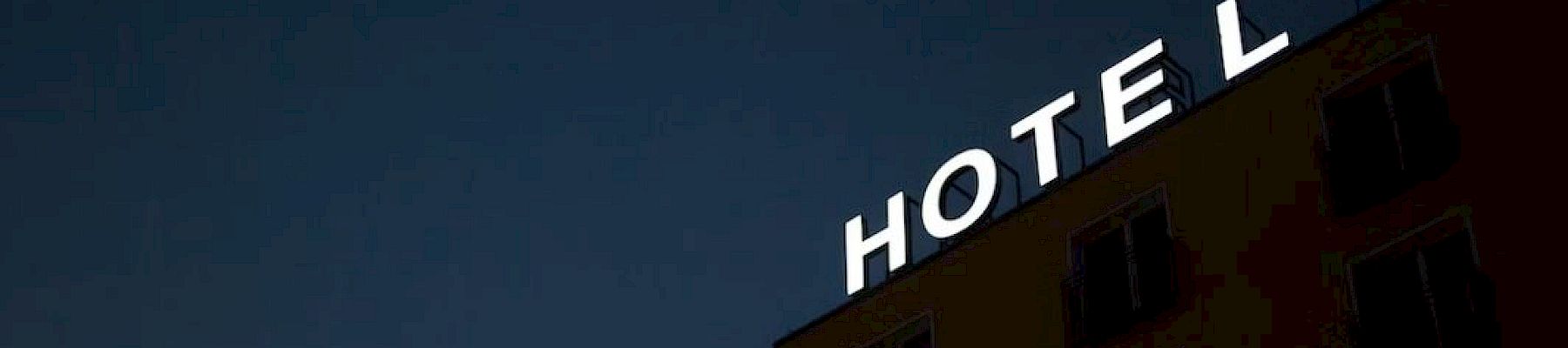 A glowing HOTEL sign atop a dark brick building, with night sky behind it.