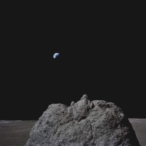 A small blue planet hovers above a dark rocky mound against a vast black background.
