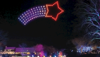 A giant lighted star-shaped display in the night sky above fireworks and a festival crowd.