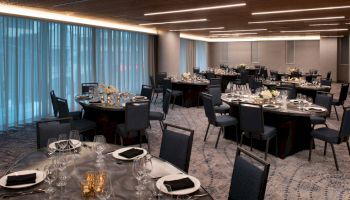 A decorated conference banquet room with tables set for a formal meal, featuring glassware and floral centerpieces on each place setting.