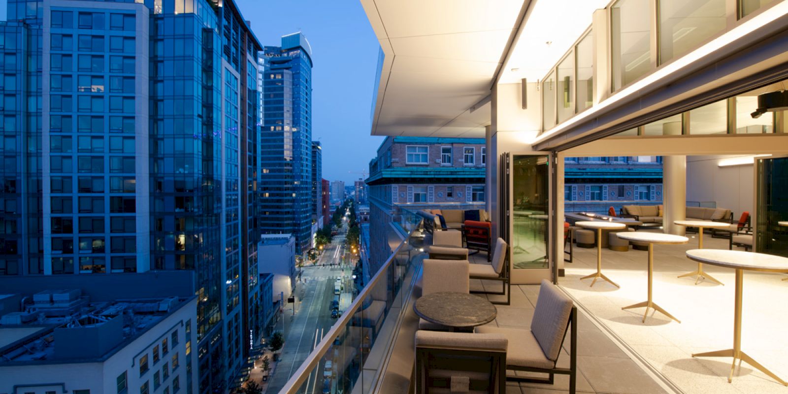 Balcony terrace with lounge chairs overlooking tall city buildings at dusk.