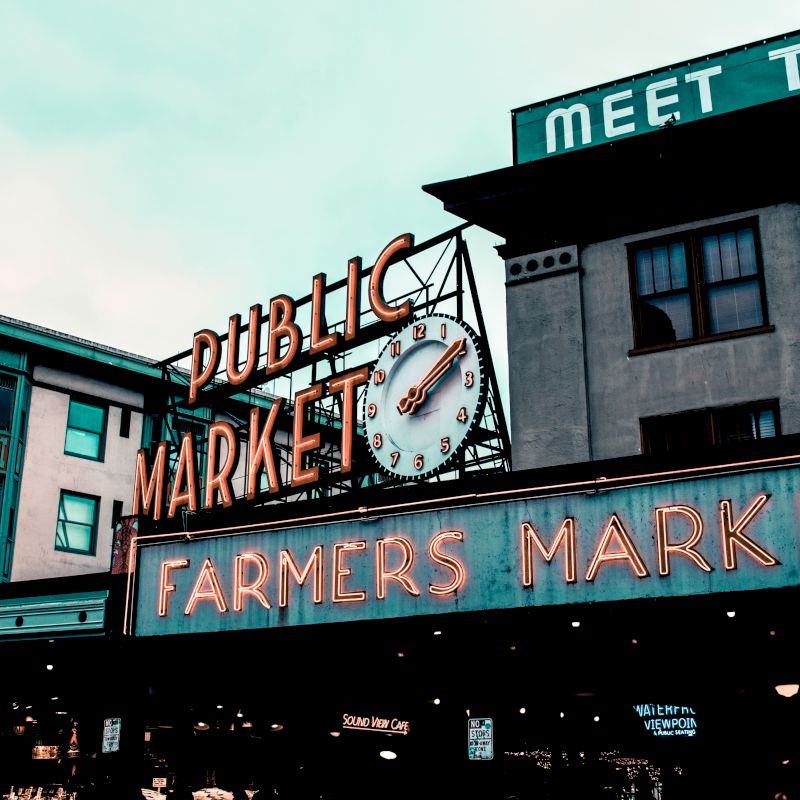 A neon-lit building sign reads &ldquo;DUBLINIC&hellip; MARKET&rdquo; with &ldquo;FARMERS MARKET&rdquo; below, plus a large clock and &ldquo;MEET THE&rdquo; marquee.