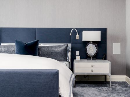 A modern bedroom with a bed, blue headboard, pillows, and a bedside table featuring a lamp, clock, and decorative tray.