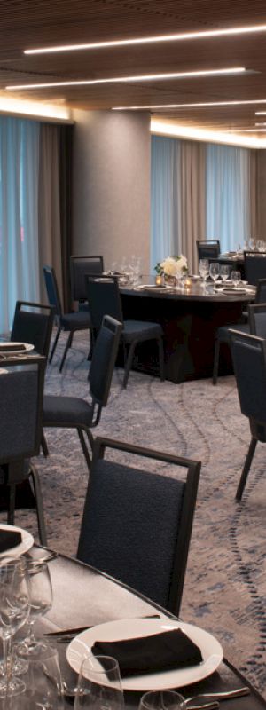 A modern banquet hall with round tables set for a formal dinner, lit by long ceiling lights and blue curtains.