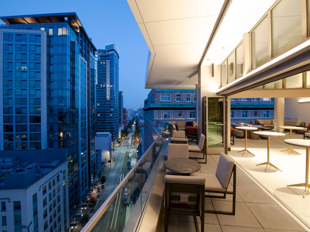 Modern rooftop terrace with lounge chairs and a view of tall downtown buildings at dusk.