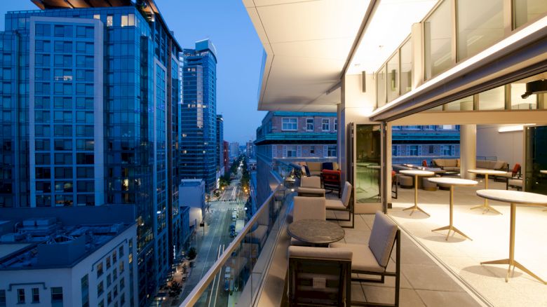 Modern rooftop terrace with lounge chairs and a view of tall downtown buildings at dusk.